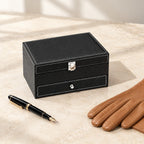 Two-tier 4-slot watch and jewelry box in black faux leather closed, beside a fountain pen and leather gloves