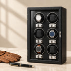 Black 6-watch winder cabinet closed, beside a fountain pen and leather gloves