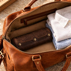 Leather watch roll packed in a weekender bag beside folded shirts