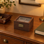 Walnut watch box on a chest of drawers, beside a leather tray and a book