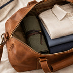 Rolled canvas watch roll in a leather weekender bag beside folded shirts