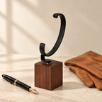 Empty walnut watch hook stand beside a fountain pen and leather gloves