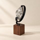 Walnut block watch stand with a black metal hook holding a steel watch