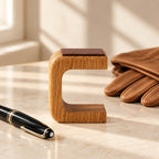 Empty wooden C-shaped watch stand beside a fountain pen and leather gloves