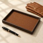 Woven valet tray with a dark wood-grain frame, beside a fountain pen and leather gloves